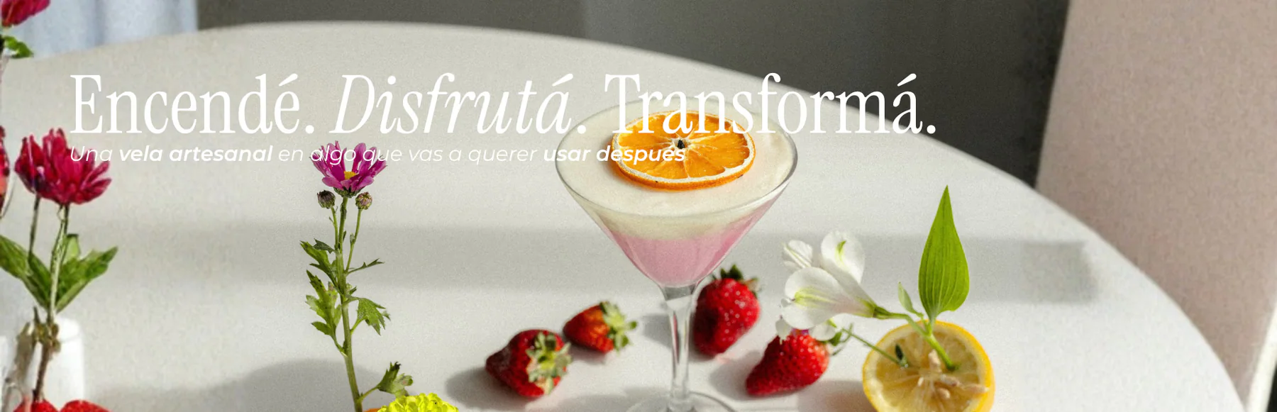 Vela en copa con rodaja de naranja, frutas y flores sobre una mesa. Encendé. Disfrutá. Transformá.