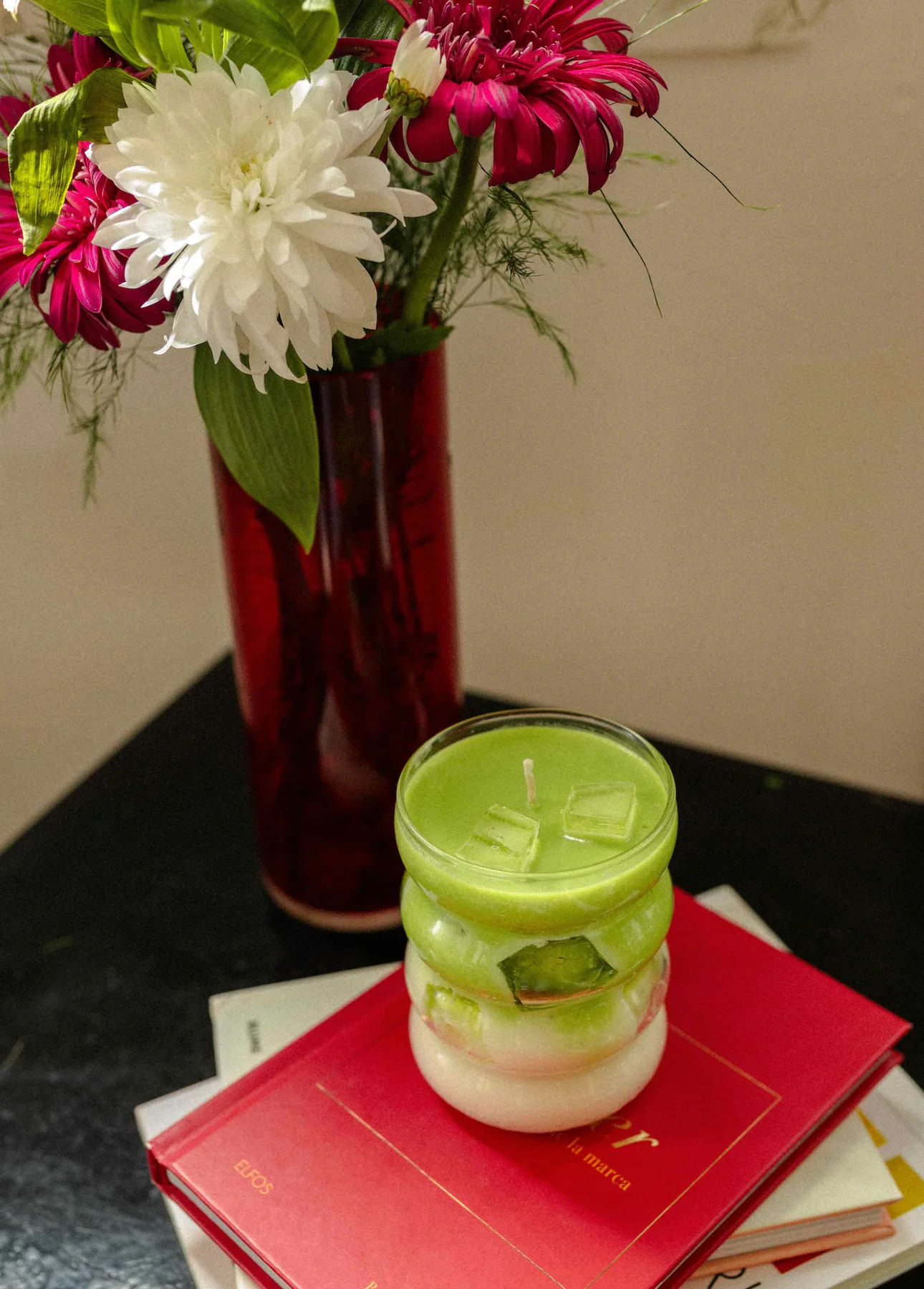 Vela Matcha Latte sobre libros junto a un florero con flores.