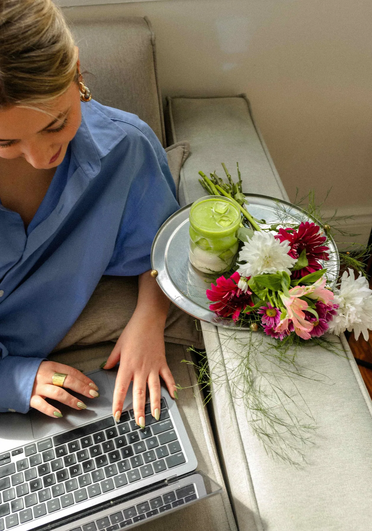 Una persona trabaja con su computadora junto a una vela Matcha Latte y flores.