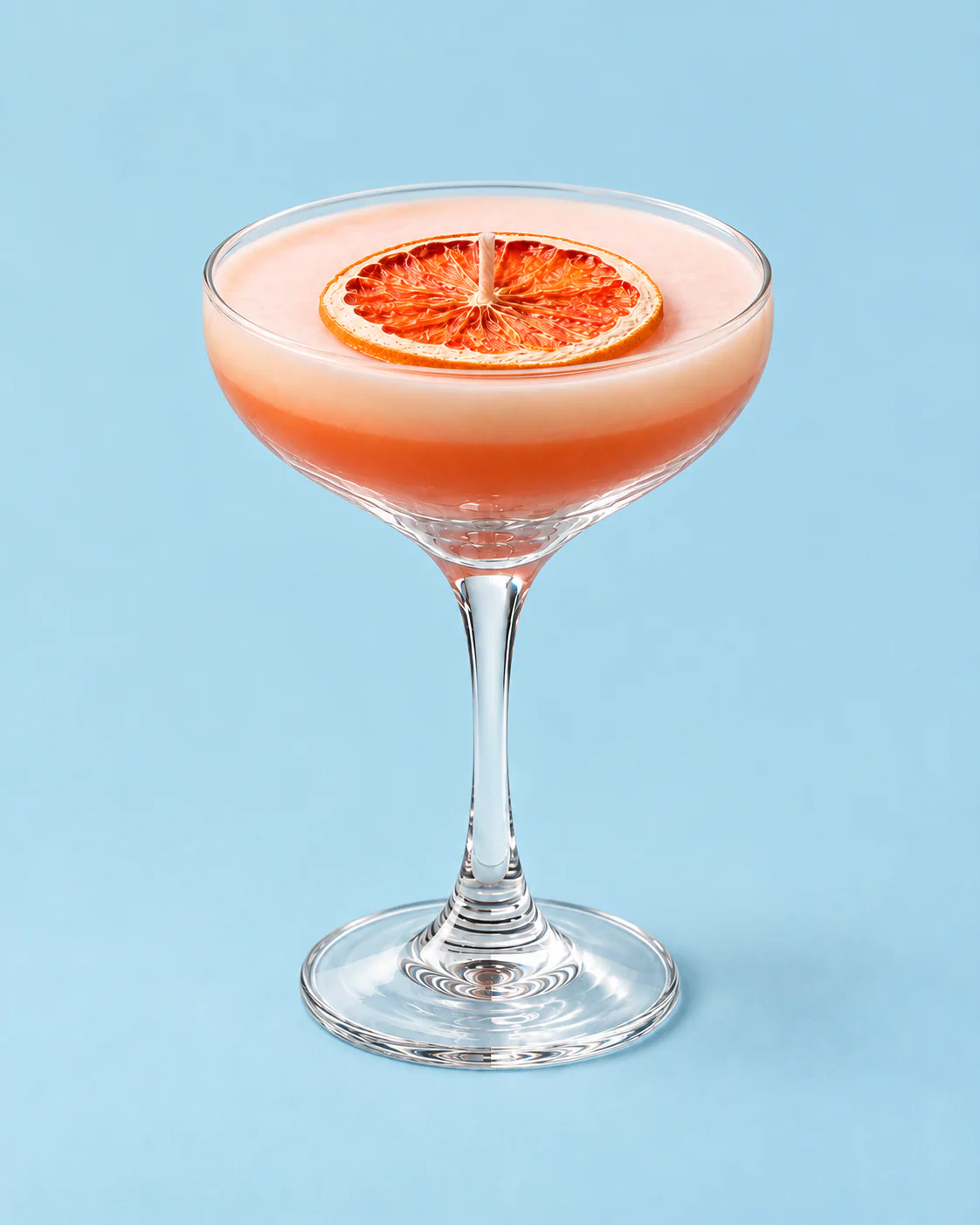 Vela Mai Tai en copa con rodaja de naranja, sobre fondo celeste.