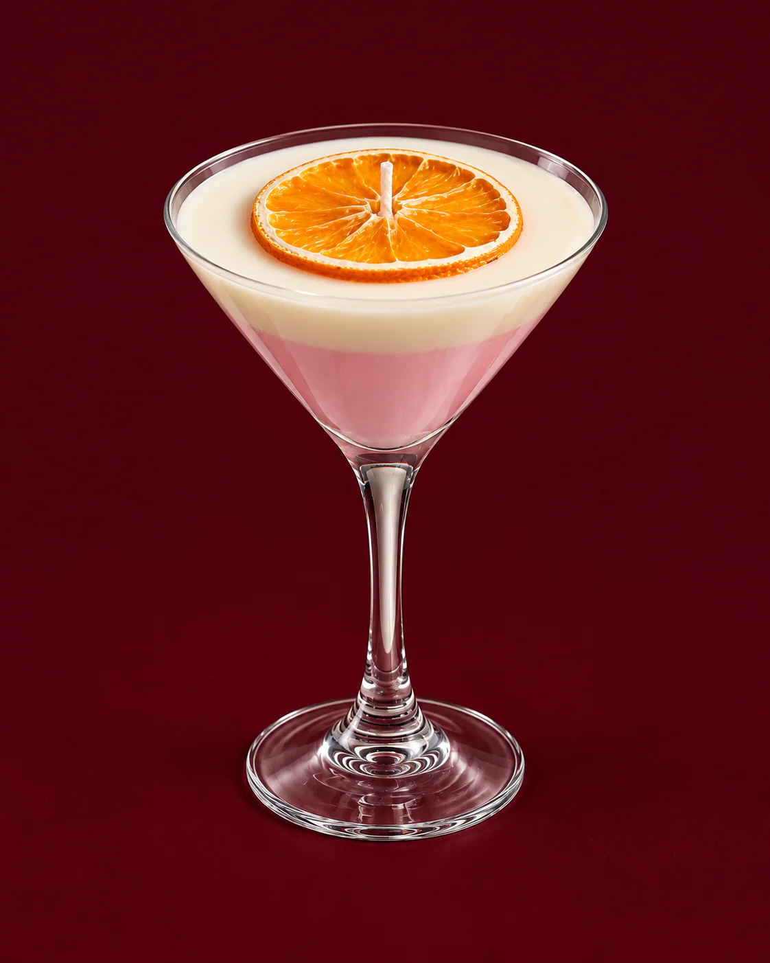 Vela Pink Martini con rodaja de cítrico en copa, sobre fondo bordó.