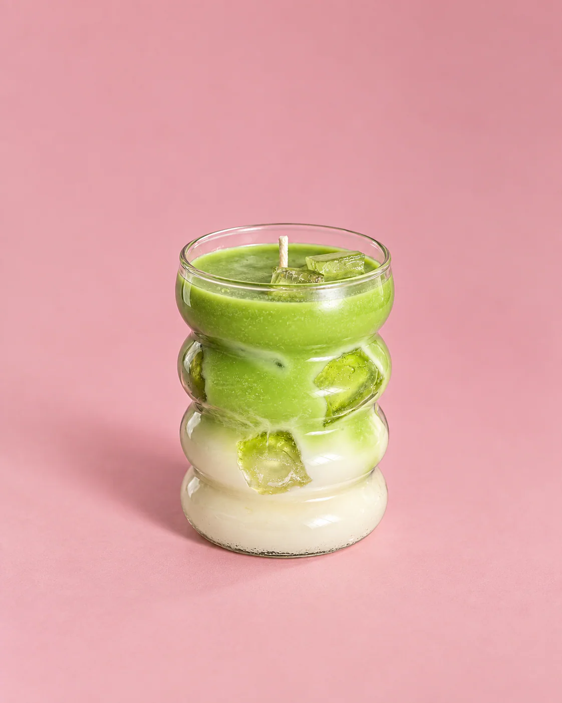 Vela Matcha Latte en vaso ondulado, sobre fondo rosa.