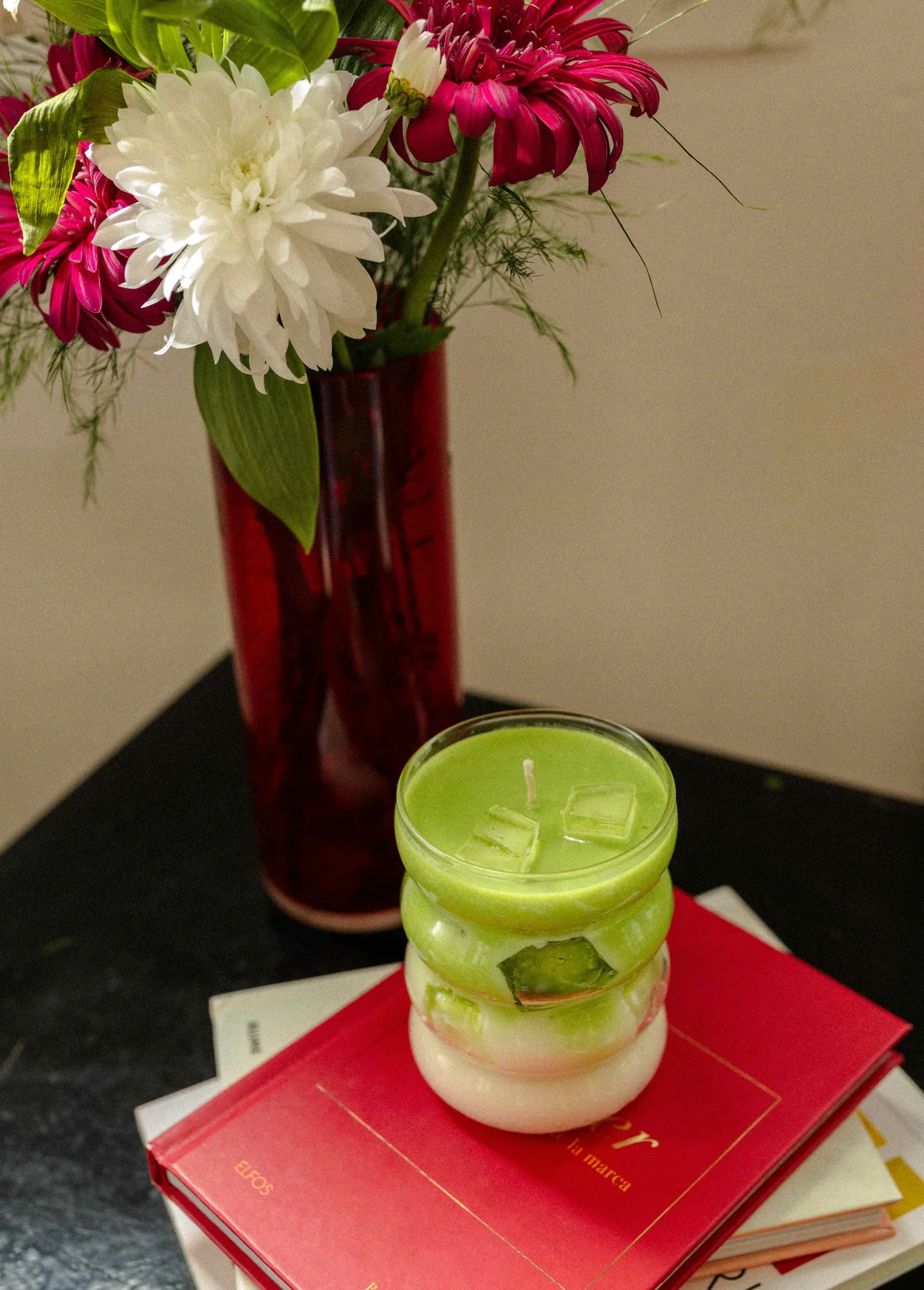 Vela Matcha Latte sobre libros junto a un ramo de flores.