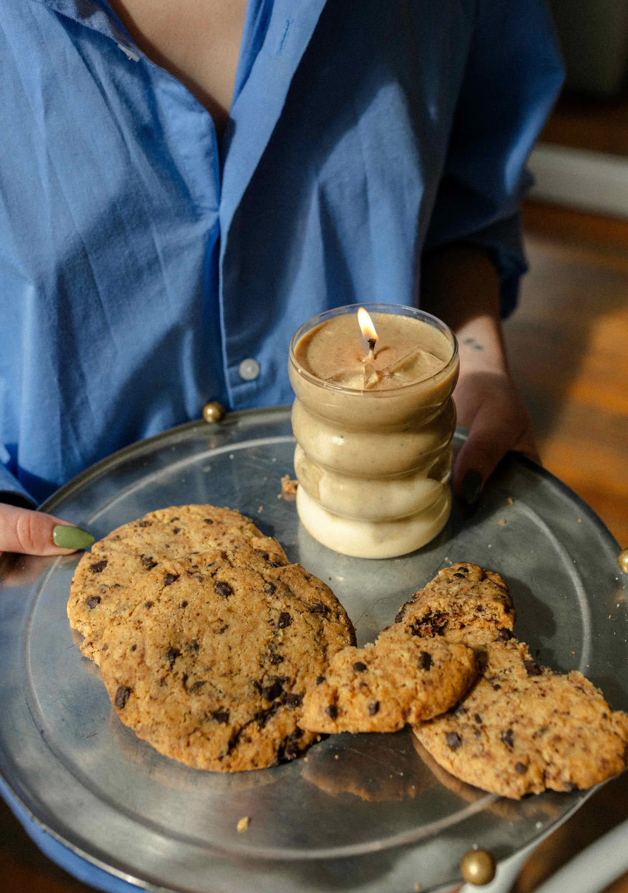 Vela Iced Coffee junto a galletitas sobre una bandeja sostenida por una persona.